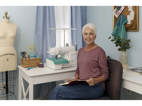 A woman sits at a white desk with a Baby Lock Applaud serger.