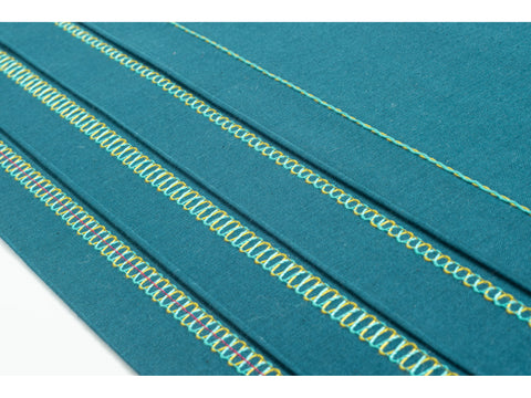 A teal fabric swatch displays various decorative stitches in yellow, blue, and pink thread.