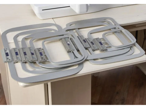 A set of ten gray rectangular embroidery hoops with metal clips on a light-colored table.