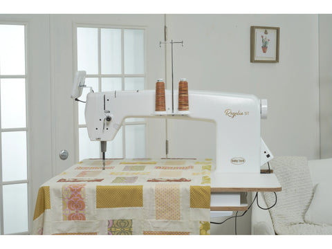 A white Baby Lock Regalia ST quilting machine with two spools of brown thread sits on a table.