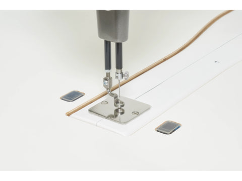 A close-up of a sewing machine needle and presser foot on a white table.