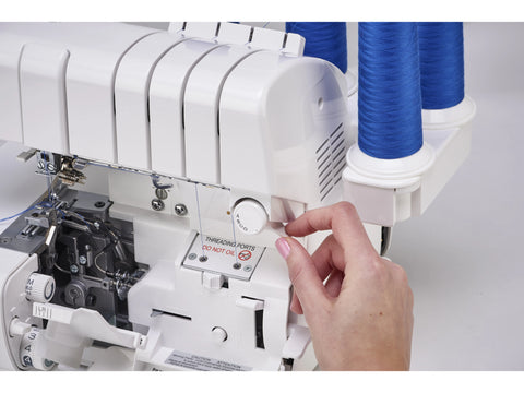 A person's hand adjusts a white Baby Lock Victory serger with blue thread spools.