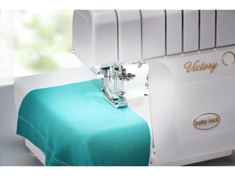 A white Baby Lock Victory serger with a teal fabric swatch under the presser foot.