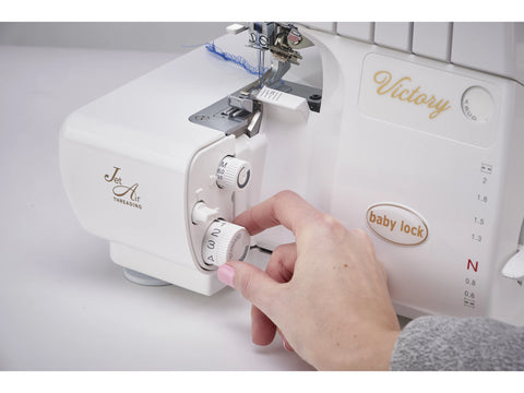 A white Baby Lock Victory serger with a hand adjusting a dial.