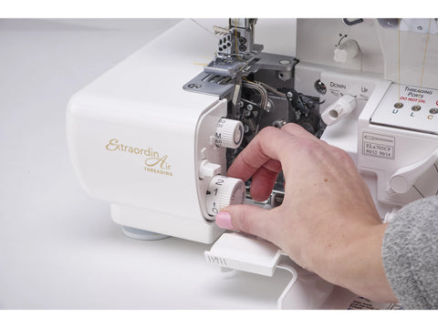 A person's hand adjusts a dial on a white Baby Lock Accolade serger.
