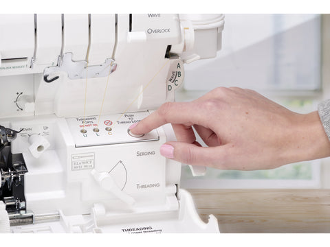A hand presses a button on a white Baby Lock Accolade serger.