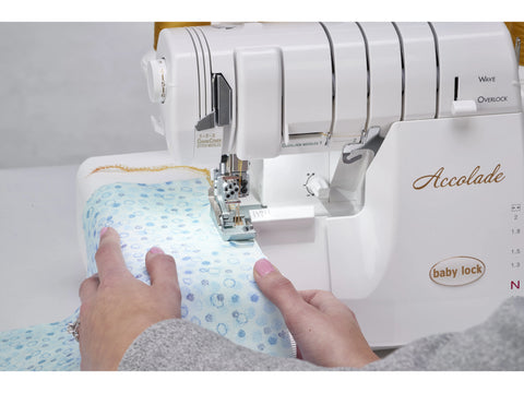 A person's hands guide light blue patterned fabric through a white Baby Lock Accolade serger.