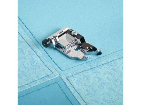 A silver 1/4" quilting foot with a black guide rests on light blue fabric with stitching.