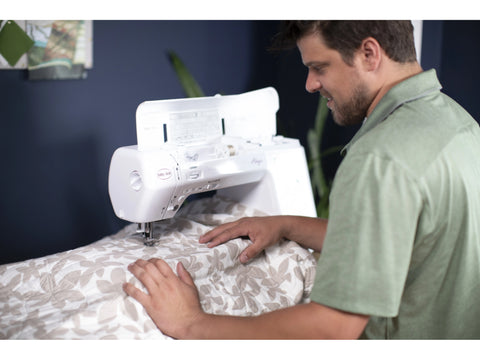 A man uses the Baby Lock Allegro Sewing & Quilting Machine to sew a patterned quilt.