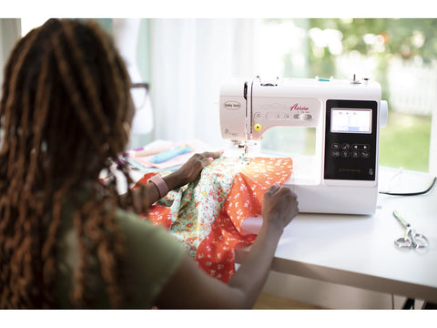 Baby Lock Aurora sewing and embroidery machine in white, used by a person with dreadlocks.