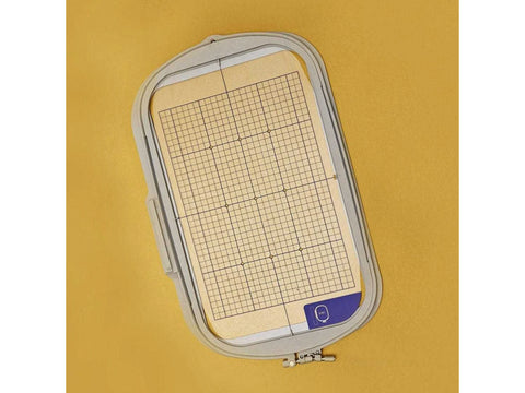 An embroidery hoop with a grid pattern is displayed on a yellow background.