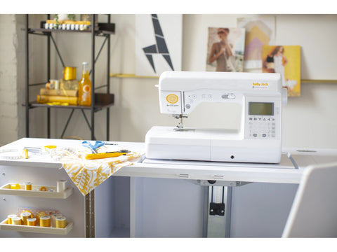 A white Baby Lock Brilliant sewing machine sits on a white sewing table.