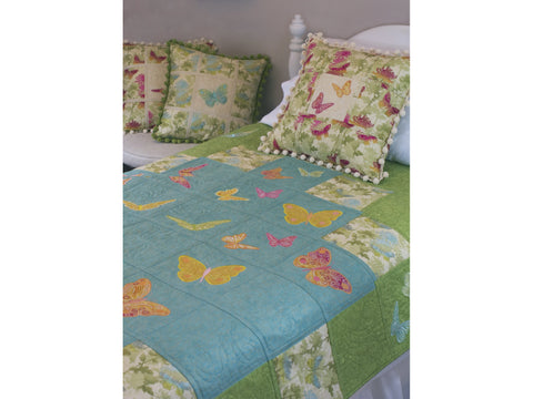 A bed is adorned with a quilt and pillows featuring butterfly designs.