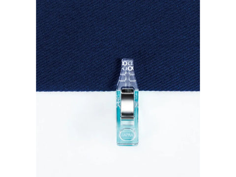 A single blue mini wonder clip holds together two pieces of fabric, one white and one navy.