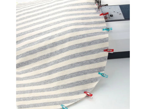 A striped fabric is held by several colorful clips next to a sewing machine.