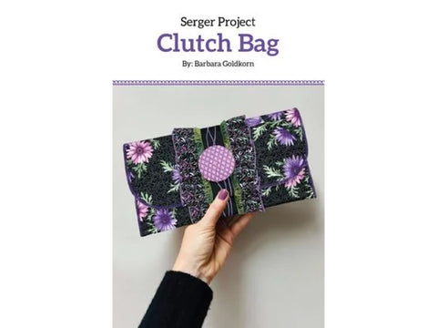 A hand holds a black clutch bag with purple and pink floral patterns.