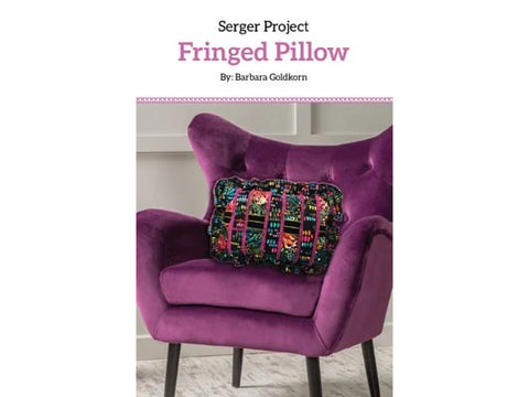 A fringed pillow with a colorful pattern rests on a purple velvet armchair.