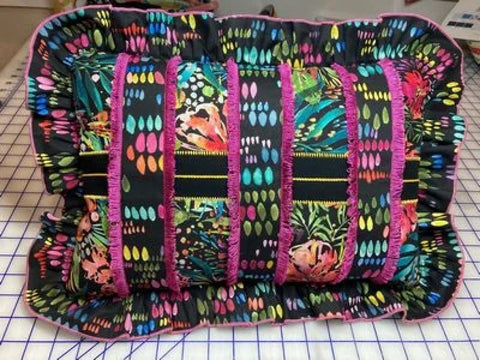 A black pillow with colorful abstract patterns and pink fringed accents.