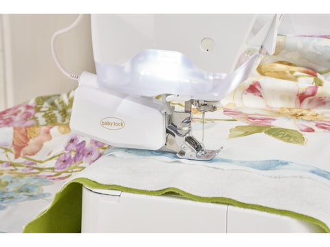 A white Baby Lock sewing machine with a bright light illuminates fabric with a floral pattern.