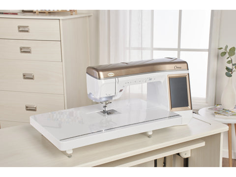 A white and bronze Baby Lock Chorus sewing and quilting machine sits on a light wood table.