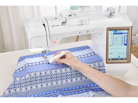 A person uses a sensor pen on blue patterned fabric with a Baby Lock Chorus sewing machine.
