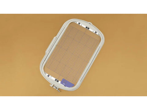 A white embroidery hoop with a grid insert is displayed on a tan background.