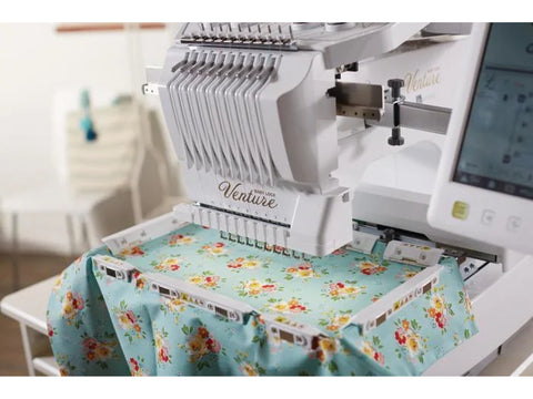 A multi-needle embroidery machine with a magnetic hoop holding floral fabric.