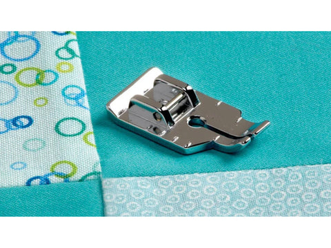 A silver 1/4" quilting foot rests on teal fabric with patterned white and blue fabric.