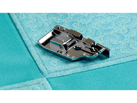 A silver 1/4" quilting foot with a guide rests on teal fabric with stitched seams.