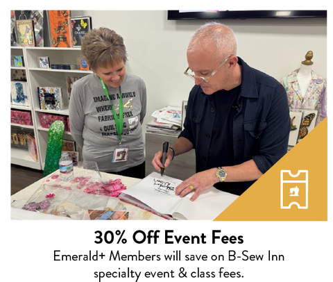 A man signs a book for a smiling woman in a sewing store.
