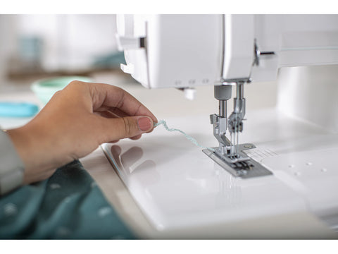 A person's hand holds light blue thread near a white Baby Lock Euphoria cover stitch serger.