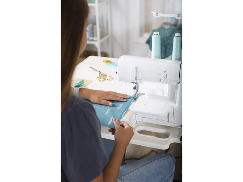 A person uses a white Baby Lock Euphoria cover stitch serger with light blue thread.