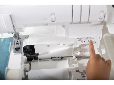 A hand presses a button on an open white Baby Lock Euphoria serger.