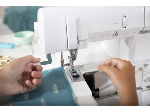 A person's hands guide fabric and thread on a white Baby Lock Euphoria serger.