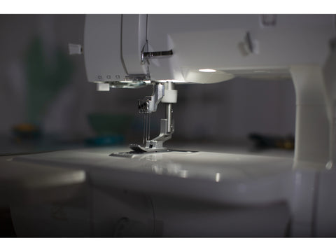 A close-up of a white Baby Lock Euphoria cover stitch serger with illuminated needles.