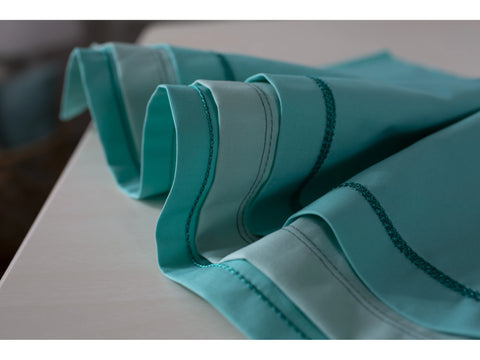 A teal fabric with decorative stitching is folded on a light surface.