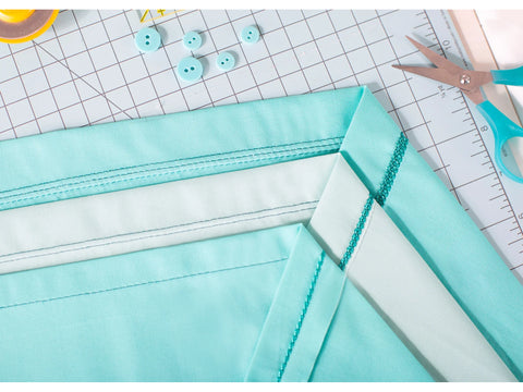 A close-up of light blue fabric with various stitches, buttons, and sewing tools.