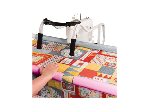 Pink quilt clips secure a colorful patchwork quilt to a white quilting machine.