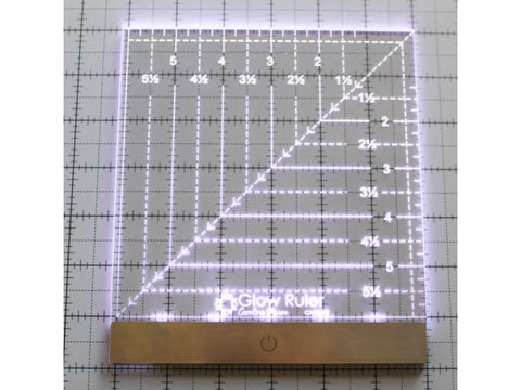 A glowing 6x6 inch clear acrylic ruler with a gold base and power button.