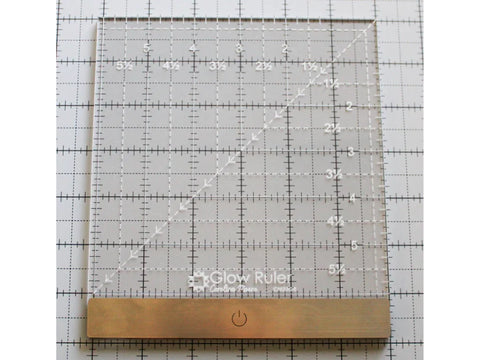 A clear 6x6 inch quilting ruler with a diagonal line and a gold base.