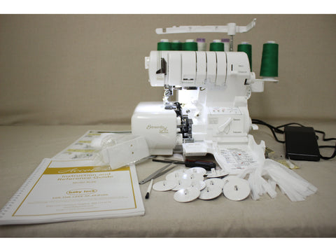 A white Baby Lock Accolade serger with green thread, manual, and accessories.
