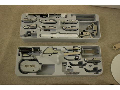 Two white trays filled with various silver sewing machine feet and accessories.
