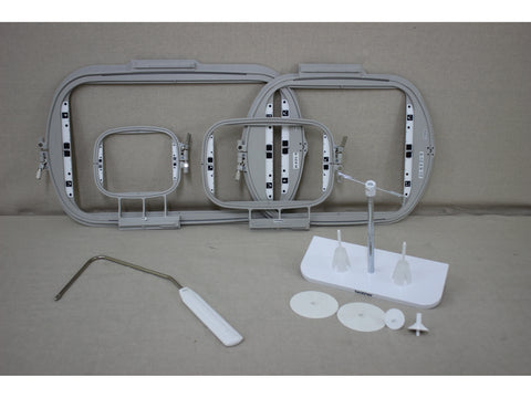 Three gray embroidery hoops, a thread stand, and a white tool are displayed on a gray surface.