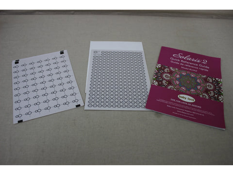 Three white and pink documents for the Baby Lock Solaris 2 sewing machine are on a gray surface.