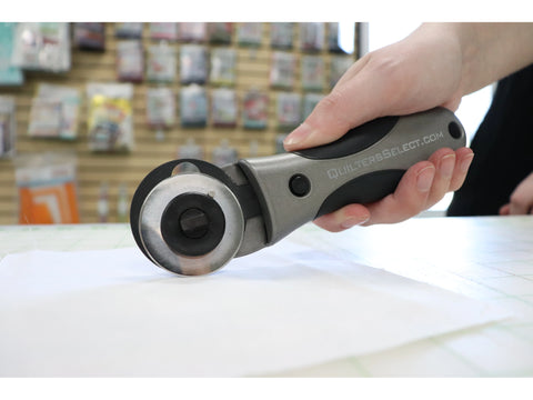 A hand holds a gray and black rotary cutter with a circular blade, poised over white fabric.