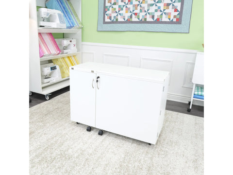 A white sewing cabinet with two doors and wheels sits on a light-colored rug.