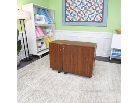 A closed wooden sewing cabinet on wheels sits on a rug in a craft room.