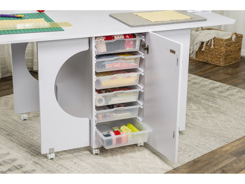 White Koala cutting table with open storage bins filled with fabric and craft supplies.