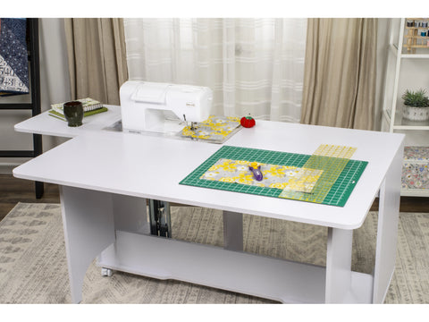 A white sewing table with a sewing machine, fabric, and cutting mat on its surface.
