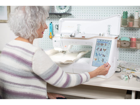 A woman uses a Baby Lock Meridian 2 embroidery machine with a large touchscreen display.